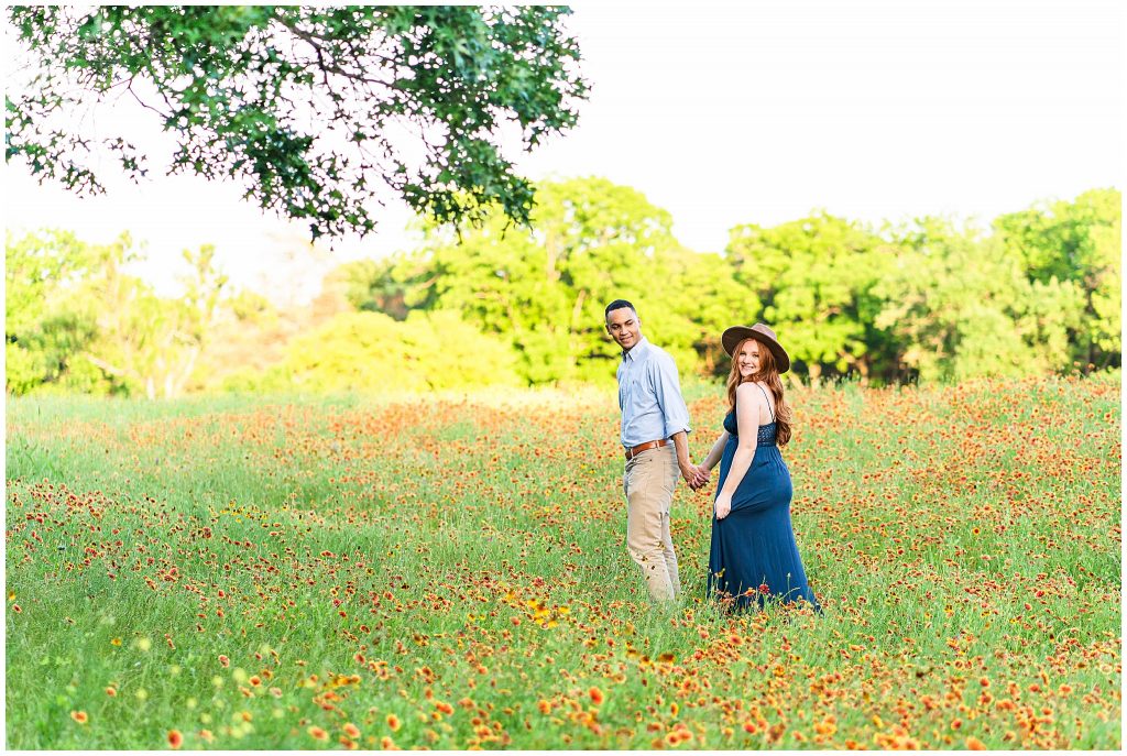 Man leading woman in boho hat in orange flower field at Cameron Park in Waco, Texas engagement photos