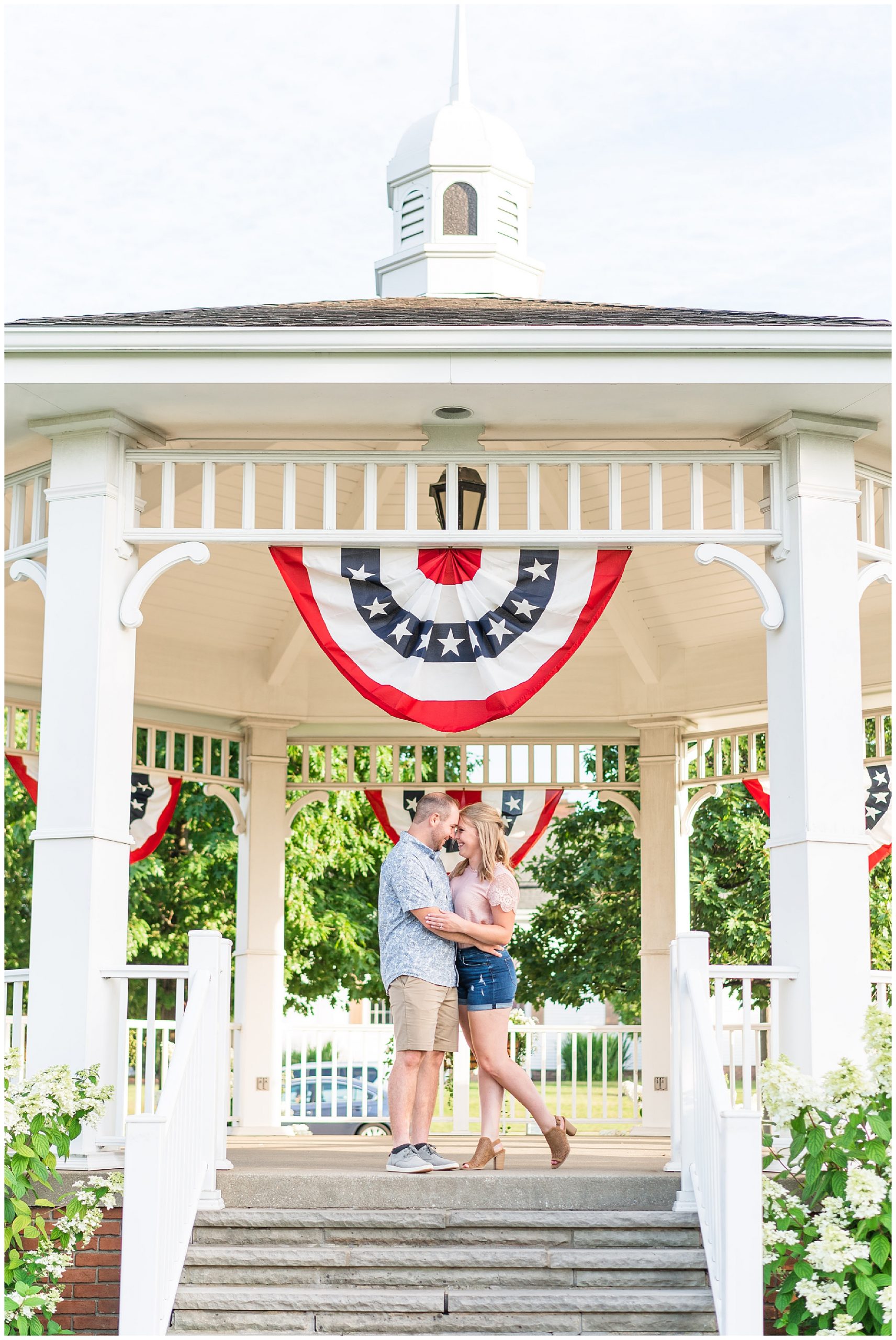 Engaged couple pose in front of summer gazebo decked in azalea bushes in Cleveland Ohio